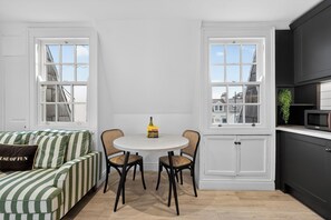 A modern kitchen with white cabinetry, a dining table with chairs, and a striped sofa. - Central Belfast Apartments Queens Lofts (Belfast)