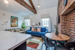 Un salon moderne avec un canapé, une table à manger et des chaises, une grande fenêtre et un mur en briques.