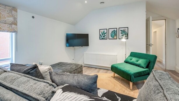 Ett modernt vardagsrum med en platt-TV, en grön soffa, grå fåtöljer och en mönstrad matta.