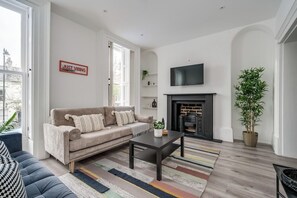 A living room with a sofa, a coffee table, a fireplace, and a television on the wall. - Central Belfast Apartments Queens Lofts (Belfast)