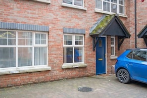 A red brick building with a blue door, a small window, and a parked blue car. - Central Belfast Apartments Somerset Mews (Belfast)