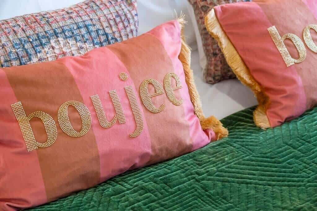 En säng med ett grönt täcke och två kuddar med broderad text.