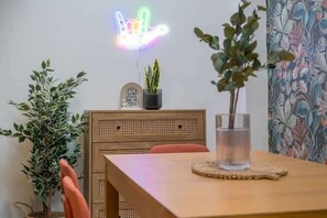 A dining area with a wooden table, a neon sign, and two potted plants. - Central Belfast Apartments Somerset Mews (Belfast)