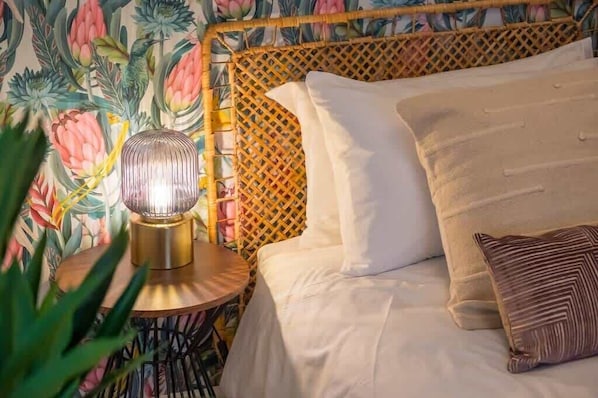 Un letto con biancheria bianca, un cuscino decorato e una lampada da comodino su un tavolino rotondo in legno.