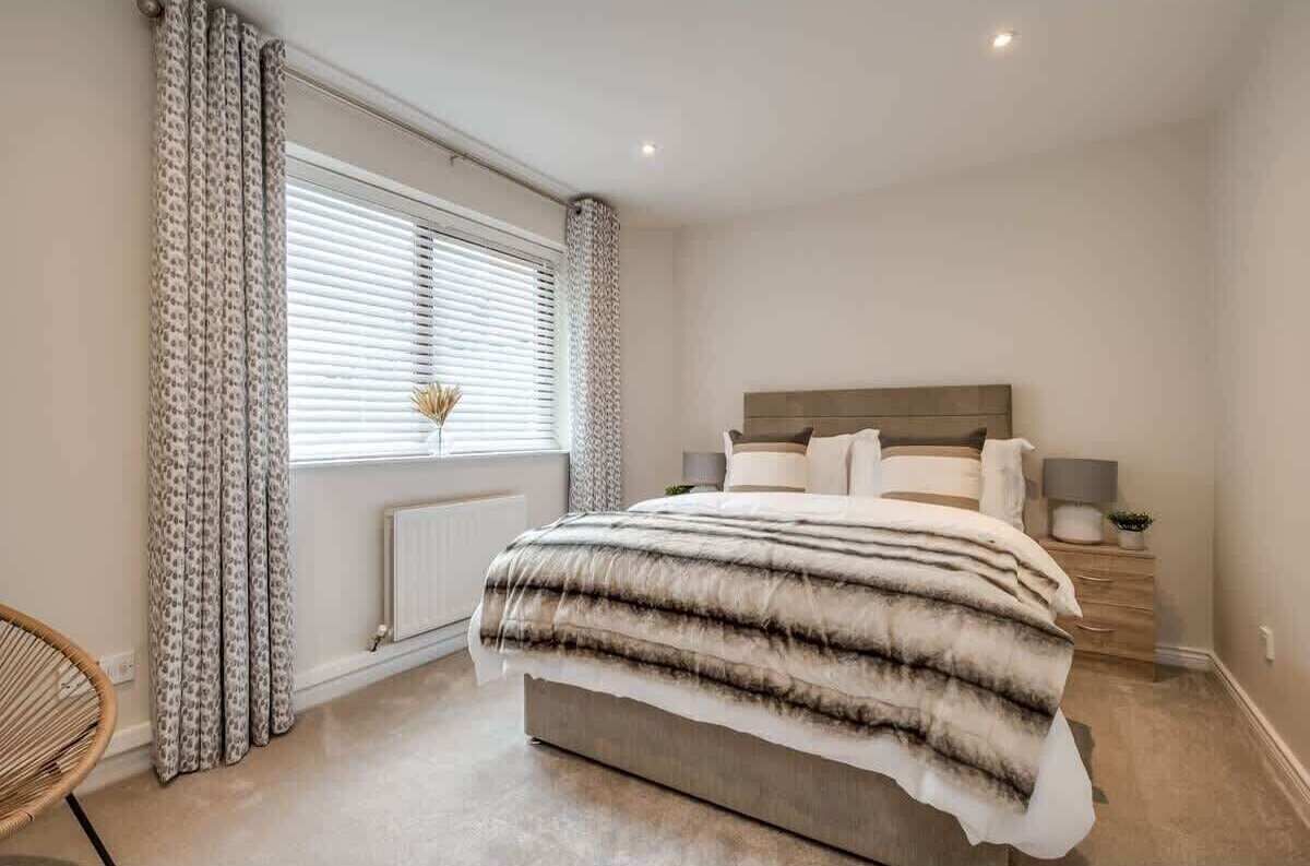 Une chambre à coucher avec un grand lit, une table de chevet avec une lampe et une fenêtre avec des rideaux.