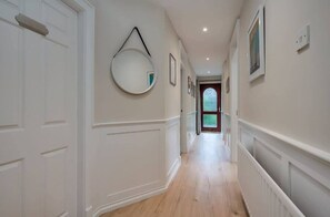 A hallway with white walls, a wooden floor, and a round mirror hanging on the wall. - Central Belfast Apartments Windsor (Belfast)