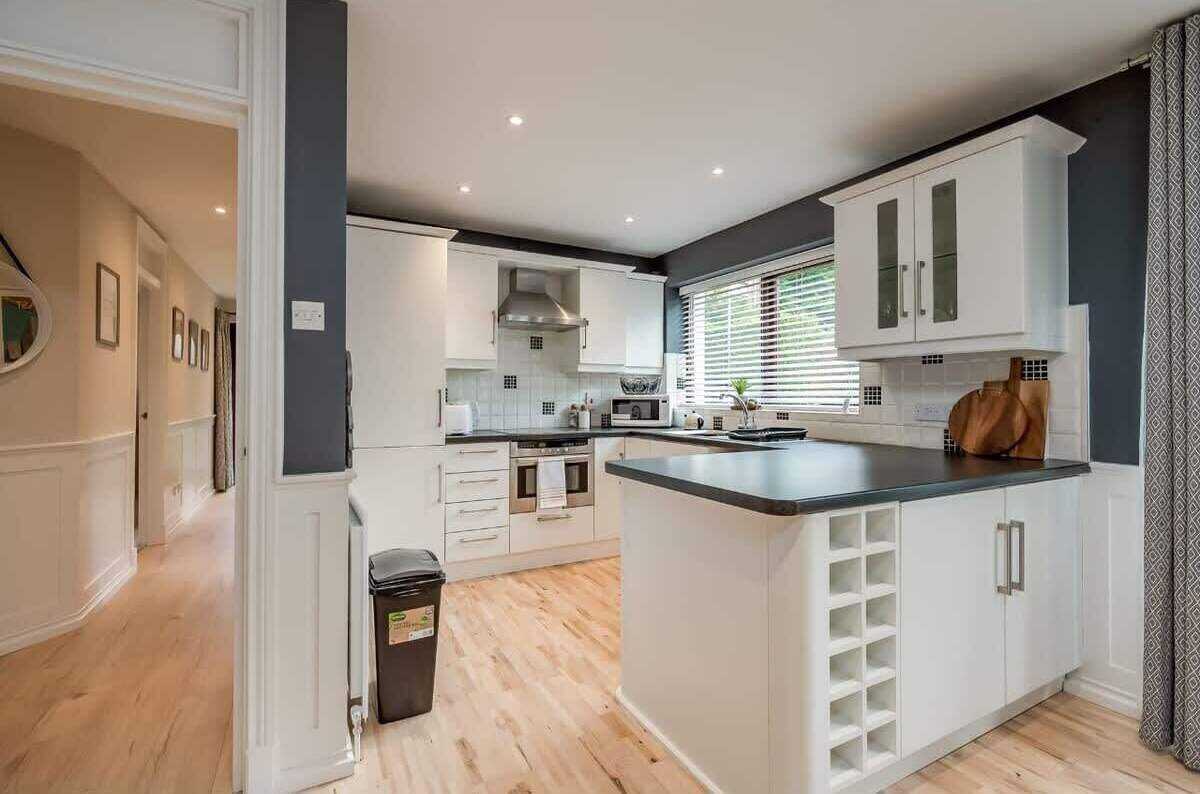 A modern kitchen with white cabinetry, a central island, and a window with blinds.