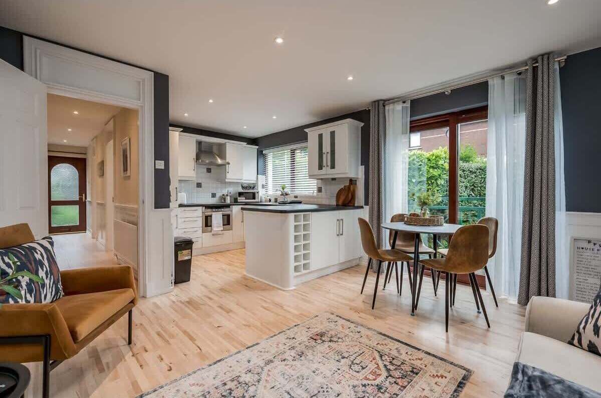 Une cuisine moderne avec des meubles blancs, un îlot central et un coin repas comprenant des chaises et une table.