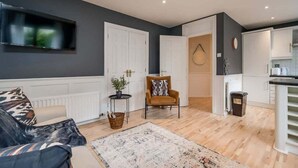 Een moderne woonkamer met een bank, fauteuil en een flatscreen televisie aan de muur.