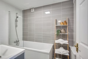 Ein modernes Badezimmer mit einer gläsernen Duschkabine, einer weißen Badewanne und einem hölzernen Ablagefach mit Handtüchern und Dekoration.