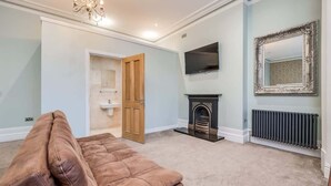 A living room with a brown sofa, a fireplace, a television, and a mirror on the wall. - Central Belfast Apartments Harpers (Belfast)