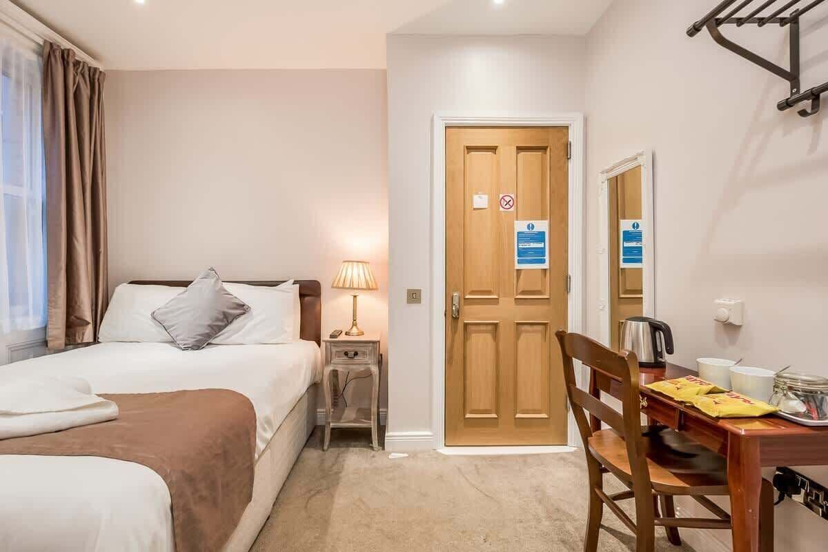 A hotel room with a bed, bedside table with lamp, wooden door, and a dining table with chairs.