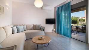 Un salón moderno con un sofá, una mesa redonda de centro, un televisor de pantalla plana y vistas al exterior.