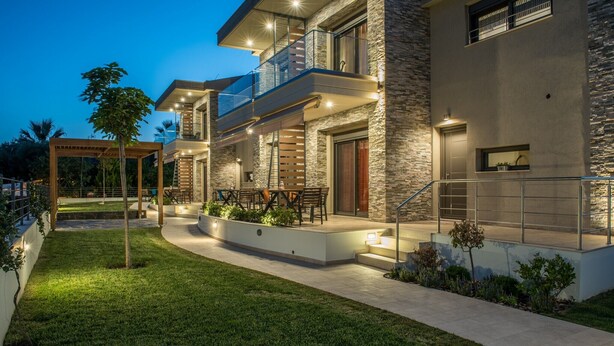 Una casa moderna de varios pisos con fachada de piedra, mobiliario exterior y un jardín bien iluminado.