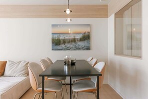 A modern dining area with a table, chairs, and a painting of a beach scene. - Stylish coastal apartment for 4 with sea view (Knokke-Heist)