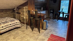 L’intérieur d’un chalet rustique comprend un lit, une table à manger avec des chaises, un coin cuisine et une vue sur l’extérieur.