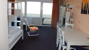Une chambre d’hôtel avec des lits superposés, un bureau, une chaise, une table, une lampe et une fenêtre avec des rideaux.