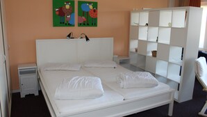 Une chambre d’hôtel avec un lit blanc, deux tables de chevet, une armoire et deux œuvres d’art murales.