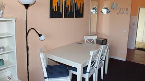 Une pièce avec une table blanche, des chaises blanches, un lampadaire, une bibliothèque et des œuvres d’art murales.