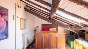 A bedroom with a wooden bed, a radiator, a painting on the wall, and a sloped ceiling with exposed beams. - A peaceful haven on Rome's doorstep (Monte dell'Ara-Valle Santa)