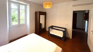 A bedroom with a bed, a dresser, a mirror, a hanging light fixture, and a window. - A peaceful haven on Rome's doorstep (Monte dell'Ara-Valle Santa)