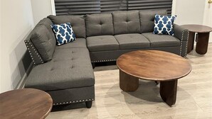 Un canapé modulable, une table basse ronde, une petite table d’appoint et un coussin à motifs.