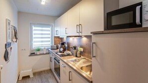 Une cuisine compacte dotée d’appareils électroménagers en acier inoxydable, d’une fenêtre avec des stores et d’un petit marchepied.
