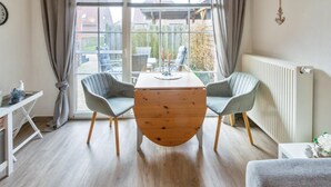 Une pièce avec une table ronde en bois, deux chaises, un radiateur et une fenêtre avec des rideaux.