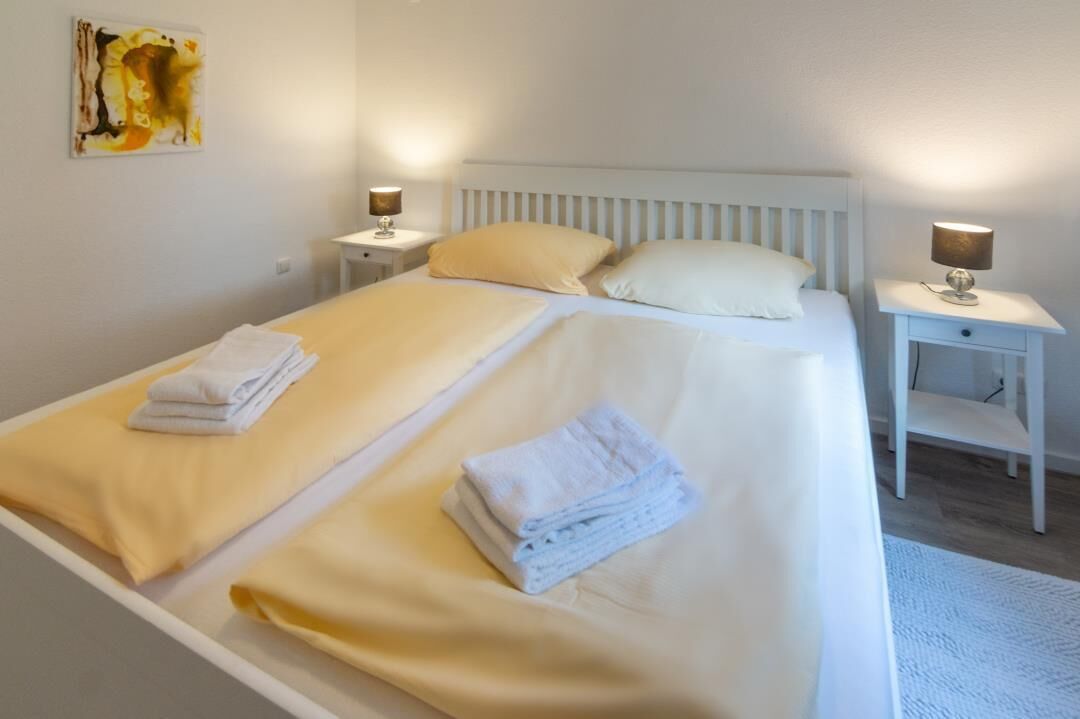 A double bed with two pillows, a bedside table with a lamp, and a painting on the wall.