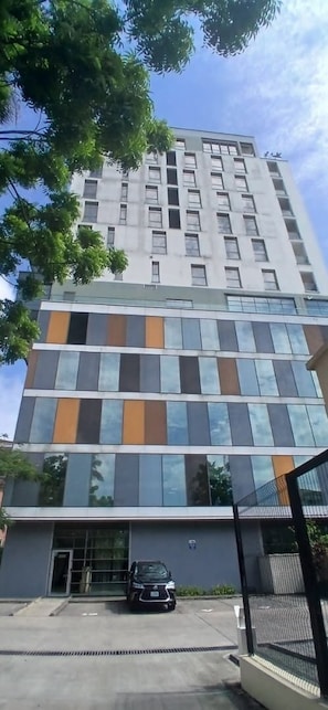 A multi-story building with a modern architectural design, featuring a mix of glass and solid panels, and a parking area in front.