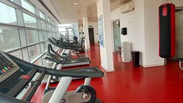 Un gimnasio con cintas de correr, un saco de boxeo y un muro con ventanas.