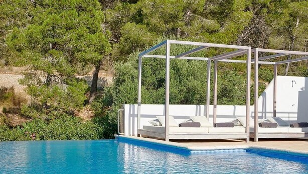 Una piscina con zona de sillones de sol y una pérgola.