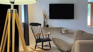 A modern living room with a sofa, a tripod lamp, a chair, and a flat-screen TV mounted on the wall. - Cosy and warm "l'Atelier des poutres" cottage (Guilliers)
