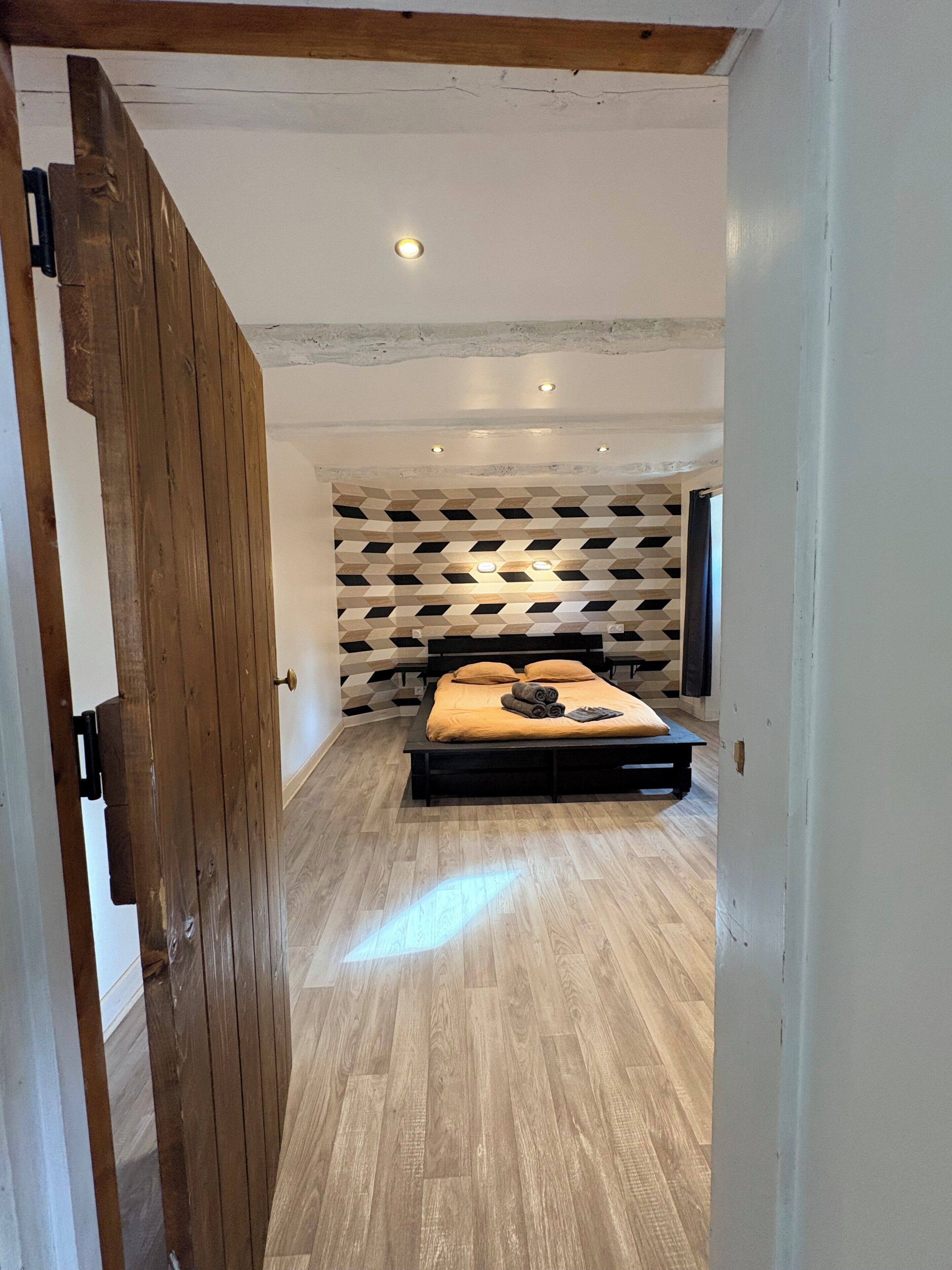 Une chambre avec un plancher en bois, un lit doté d’une tête de lit et un mur orné d’un motif géométrique.
