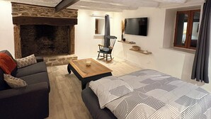 A cozy room with a fireplace, a sofa, a bed, a TV, and a stone wall. - Cosy and warm "l'Atelier des poutres" cottage (Guilliers)