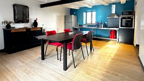 A modern kitchen with a dining area, featuring a wooden floor, a black dining table with red chairs, and a blue accent wall. - Cosy and warm "l'Atelier des poutres" cottage (Guilliers)