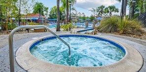 Ein Whirlpool, umgeben von Palmen, und ein Poolbereich mit Liegestühlen.