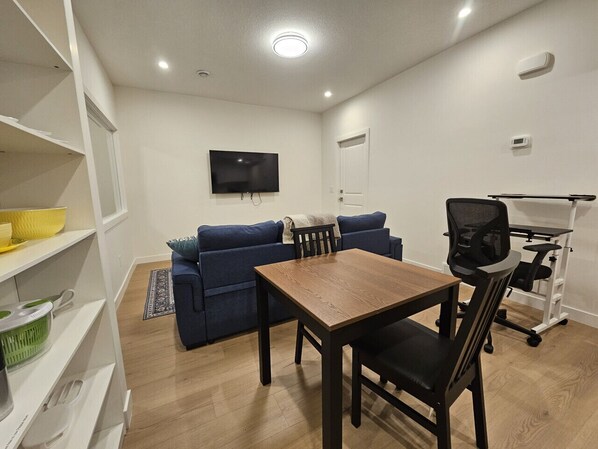 A room with a dining table, blue sofa, TV, and exercise equipment.