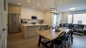 Une cuisine moderne dotée d’un îlot central, d’appareils électroménagers en acier inoxydable et d’un coin repas avec une table et des chaises en bois.
