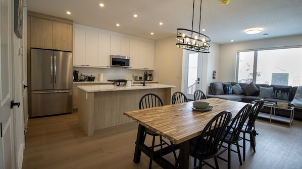 Una cocina moderna con una isla central, electrodomésticos de acero inoxidable y un comedor con mesa y sillas de madera.