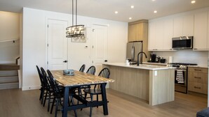 Eine moderne Küche mit Kochinsel, Edelstahlgeräten und einem Essbereich mit Holztisch und Stühlen.