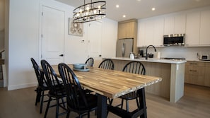 Una cocina moderna con una mesa de comedor de madera, sillas negras, una isla integrada, armarios blancos y electrodomésticos de acero inoxidable.