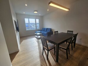 A modern living room with a dining table, blue sofa, and a view of the city through large windows. - 💎 Detached Luxury Suite: No Shared Walls + King Bed & AC (Calgary)