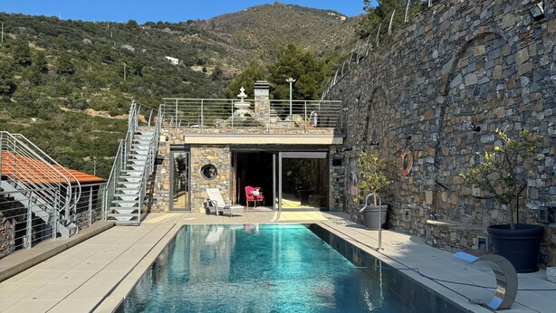 Una piscina con muretto in pietra e una scala che conduce a una zona coperta.