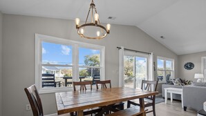 Un amplio comedor con una gran mesa de madera y sillas, una araña y ventanas grandes que ofrecen vistas al exterior.
