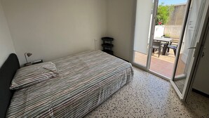 Un dormitorio con cama, escritorio, lámpara y puerta corrediza de vidrio que da a un patio exterior.