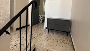 Una escalera con barandal negro que conduce a una habitación con piso estampado, un banco y un adorno circular sujeto a la pared.