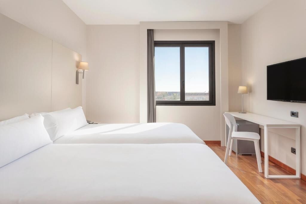 Una habitación de hotel con dos camas, un escritorio con silla, un televisor y una ventana con vistas.