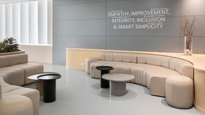 A modern lounge area with a curved sofa, two round tables, and a wall with motivational text.