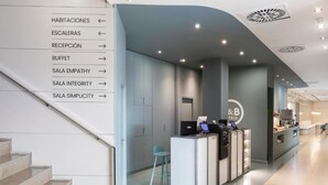 A hotel reception area with a staircase, reception desk, and directional signage.